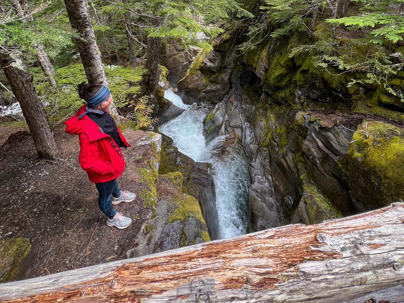 Frau am Rande einer Schlucht im Mt. Rainier National Park mit tosendem Gewässer zu ihren Füßen
