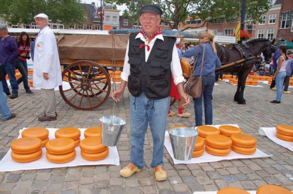 Milchbauer mit Eimer vor Käserädern in Gouda