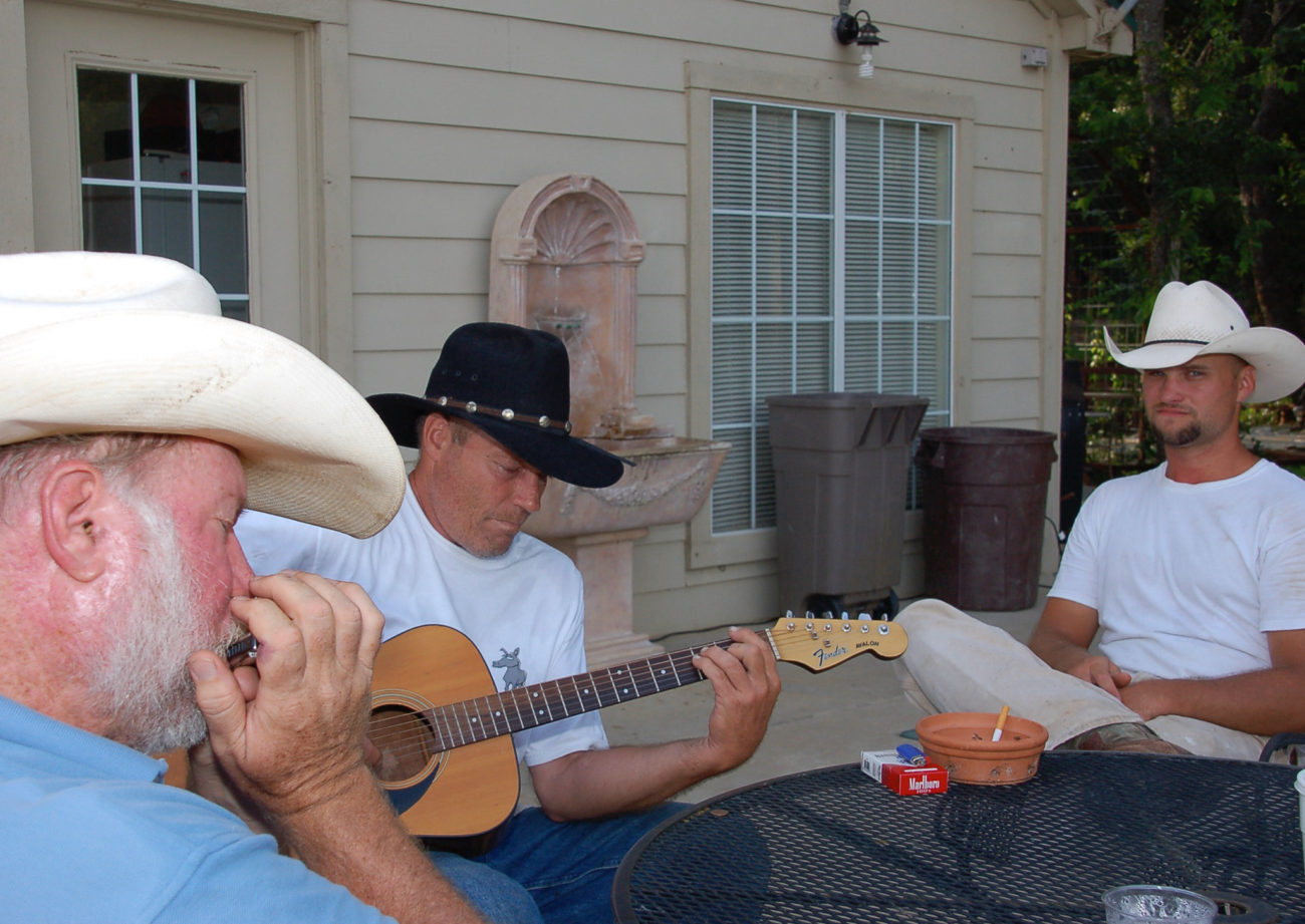 Cowboys musizieren mit Mundharmonika und Gitarre am Lagerfeuer auf der Dude Ranch in Oklahoma