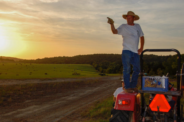 Ein Cowboy steht im Sonnenuntergang auf einem Traktor, während seiner Arbeit auf einer Dude Ranch in Oklahoma