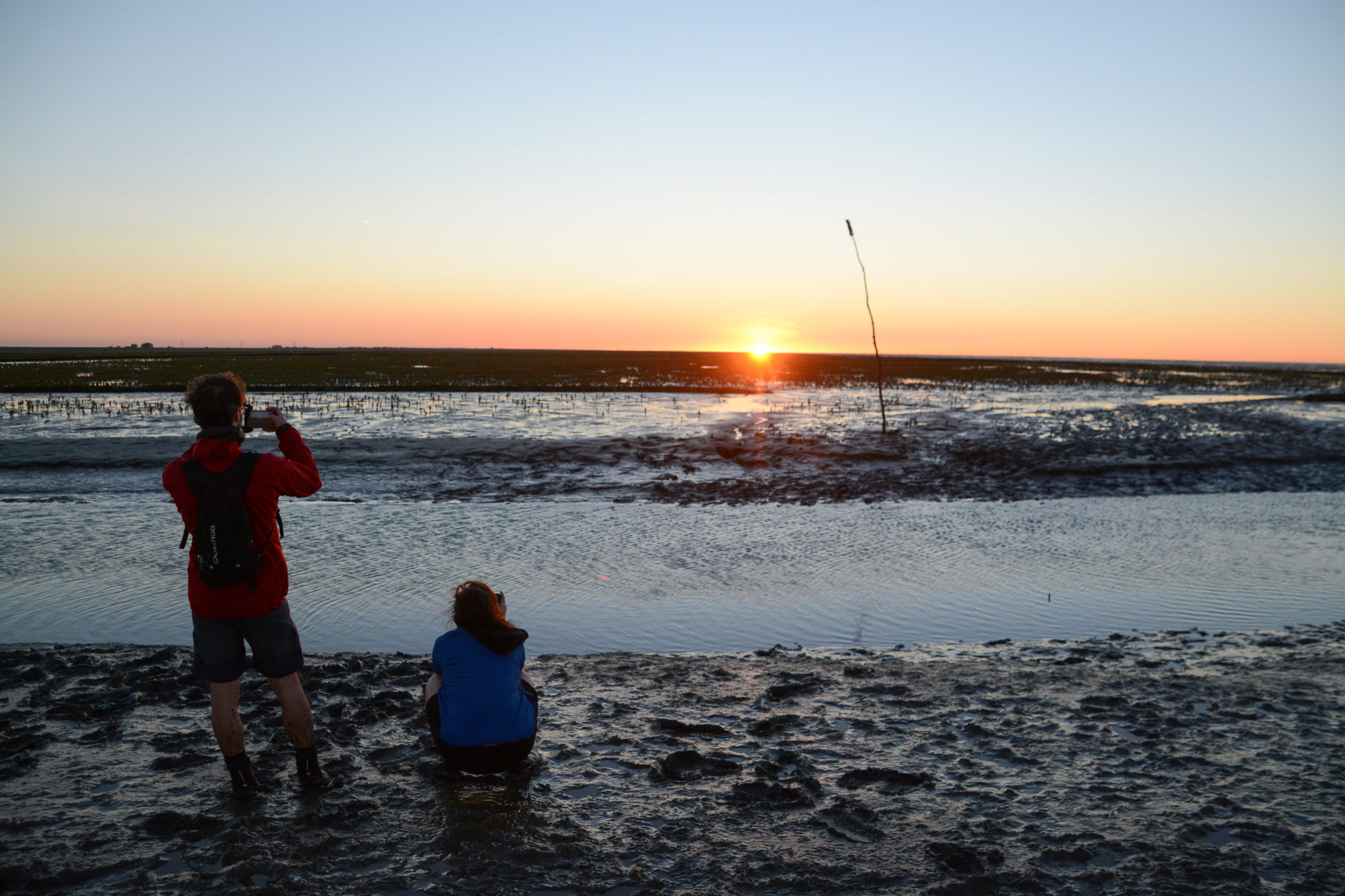 Zwei Wattwanderer fotografieren den Sonnenuntergang nach Wattwanderung in Holland