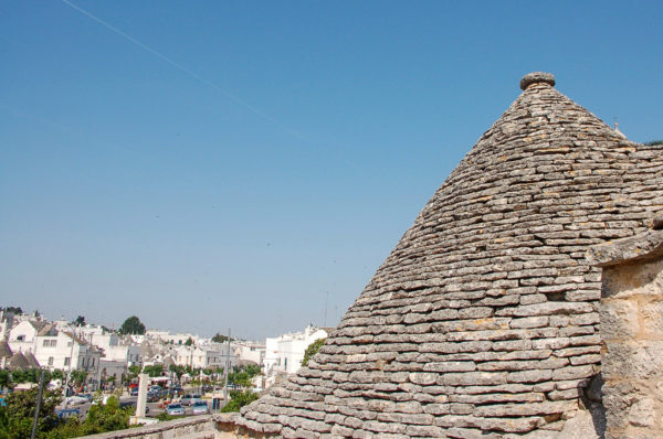 Das Dach eines Trullo in Alberobello mit Stadtansicht und Chemtrails am Himmel
