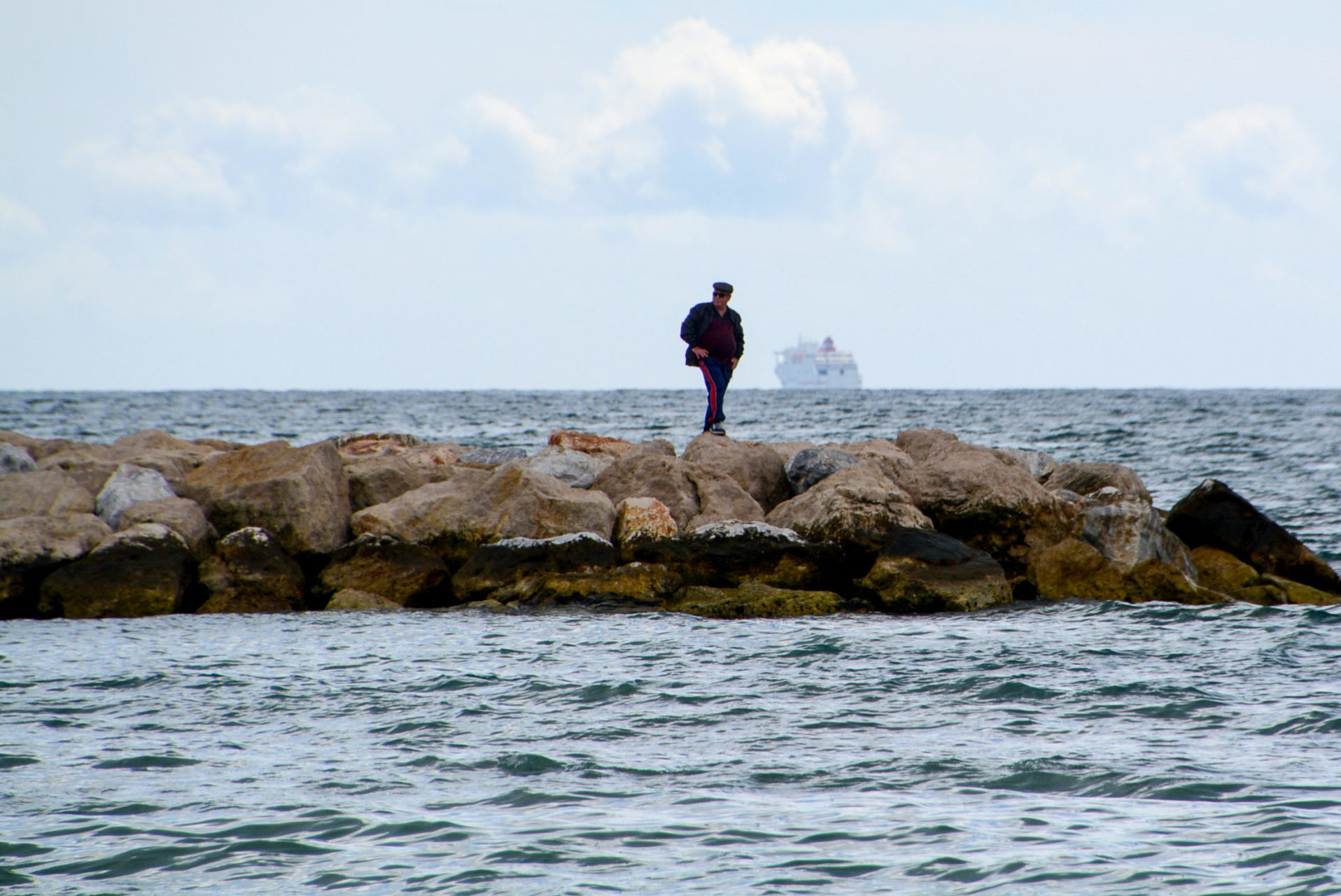 Mann auf einer Buhne am Hafen von Málaga mit Kreuzfahrtschiff im Hintergrund