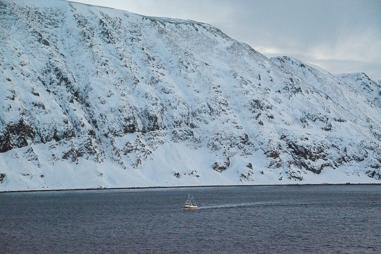 Fischkutter vor verschneiter Bergwand am Nordkapp in Norwegen