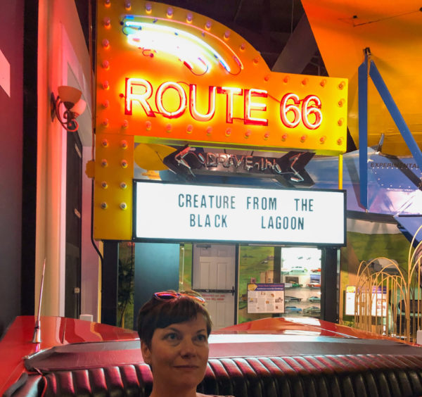 Junge Frau auf einem Kunstledersofa vor einer Leuchtreklame der Route 66