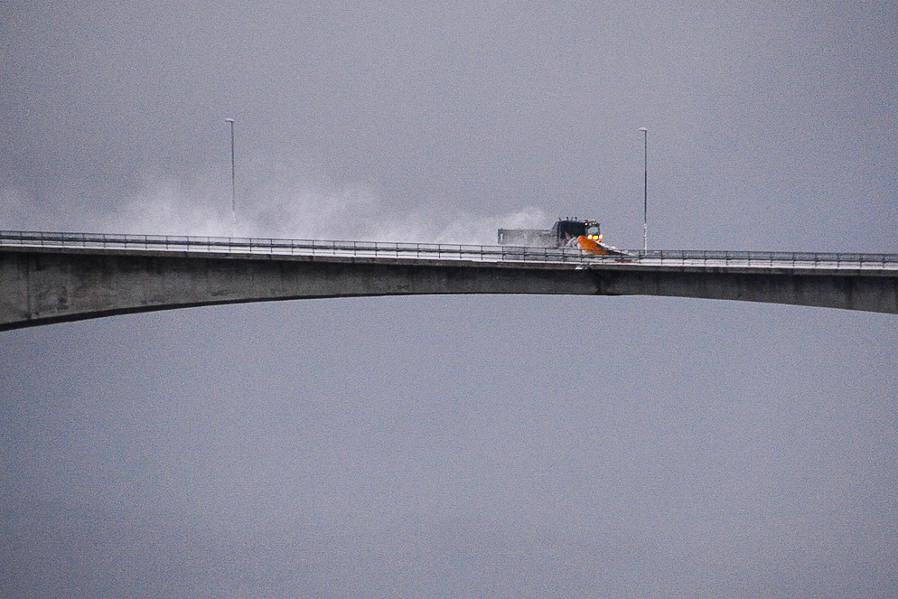 Nahaufnahmen eines Schneepflugs auf einer Brücke in Nordnorwegen mit Schiffen und Schnee
