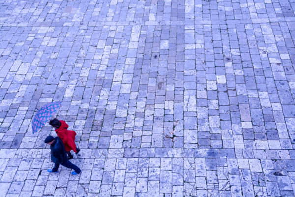 Mann und Frau mit Regenschirm auf den Steinplatten des Marktplatzes von Hvar