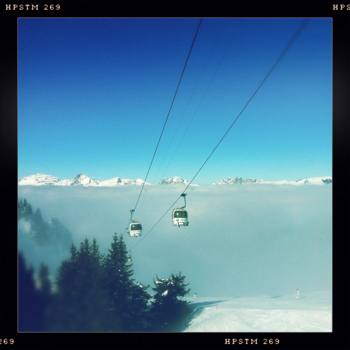 Kabinen eines Sessellifts kommen aus dem Nebel vor dem Panoramo von Eiger, Mönch und Jungfrau im Berner Oberland