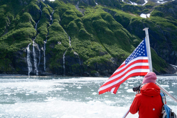 Touristen fotografiert Landschaft mit Eisschollen, Wasserfällen und amerikanischer Flagge bei Minikreuzfahrt in Alaska