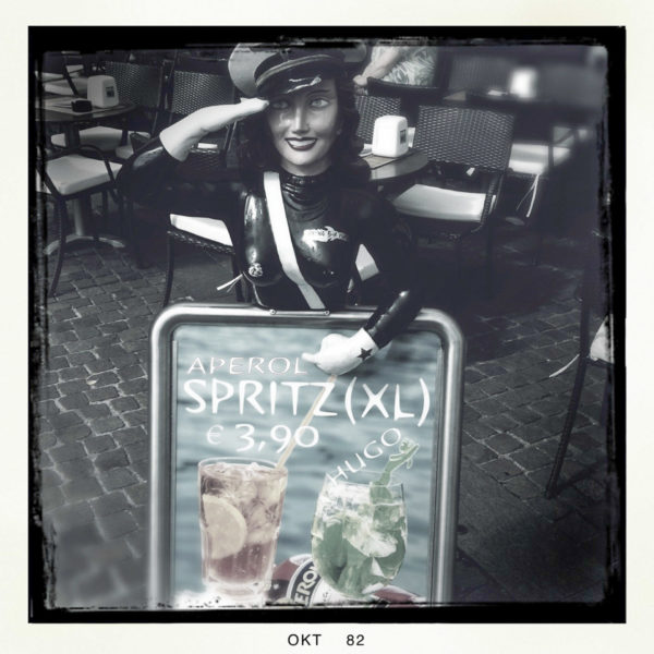 Salutierende Frau mit Reklameschild für billigen Aperol-Spritz