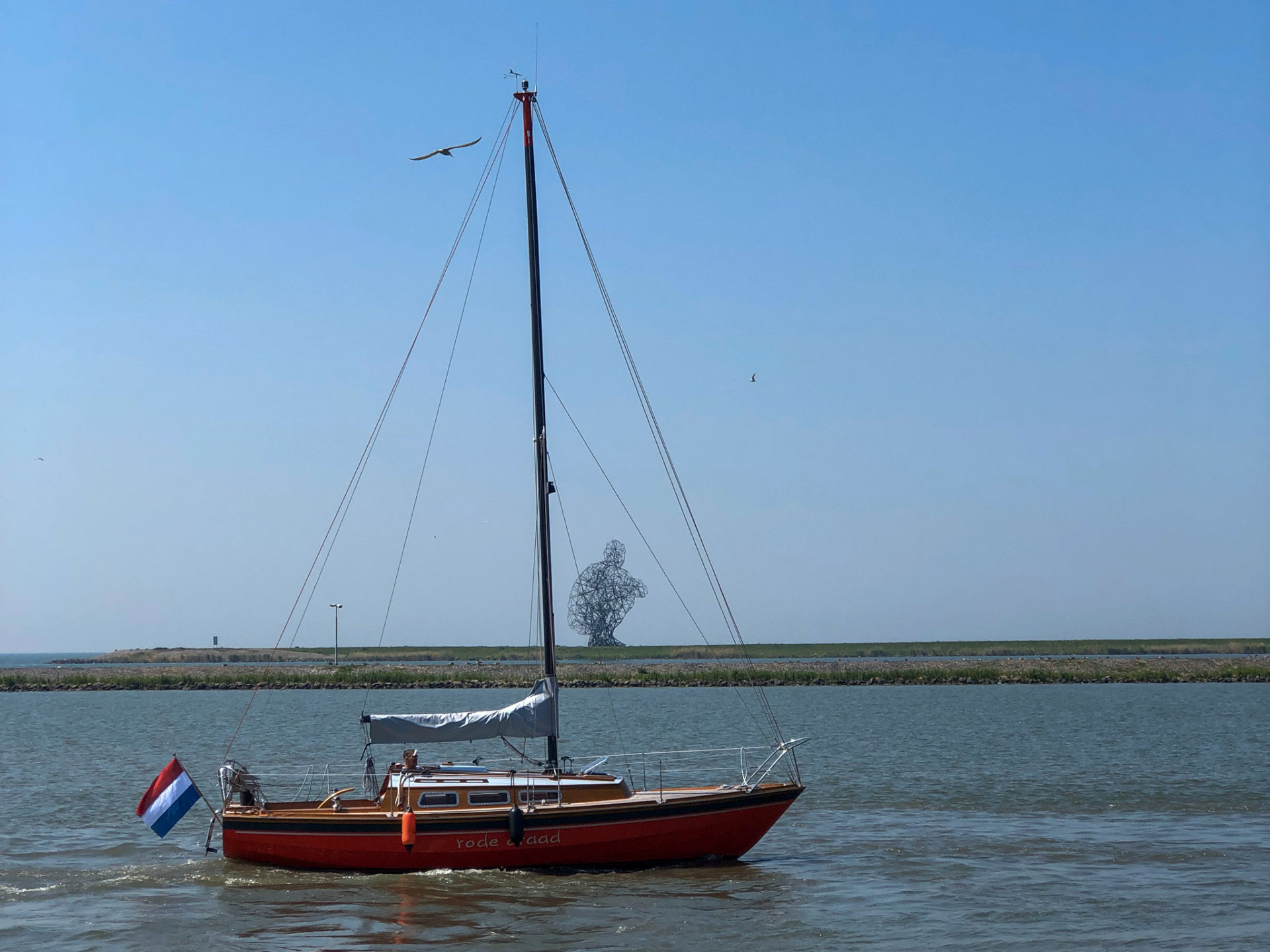 Segelboot bei der Passage eines Kanals im wasserreichen Flevoland mit Skulptur im Hintergrund
