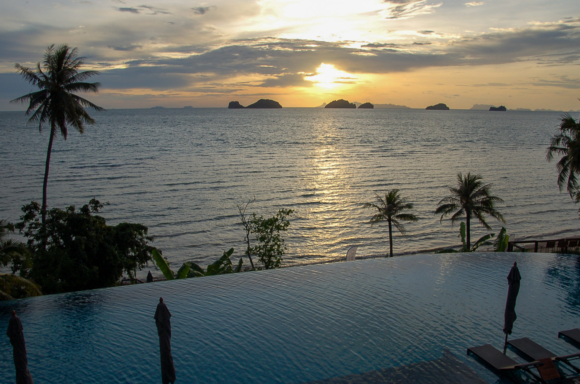Sonnenuntergang über dem Infinity Pool in Thailand mit Bergen, Meer und Palmen