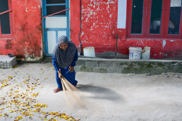 Frau fegt die Straße mit einem Besen auf Fenfushee Island auf den Malediven