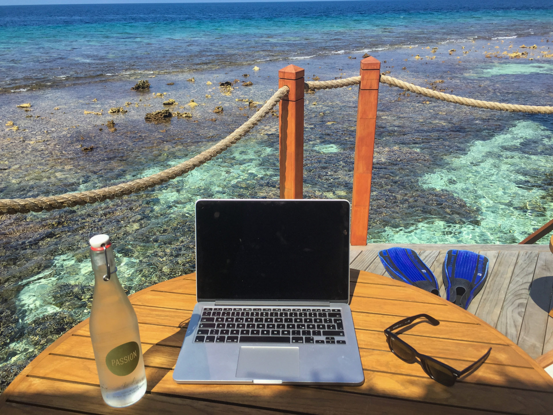 Arbeitsplatz mit Laptop, Sonnenbrille und Taucherflossen auf Korallenriff in den Malediven