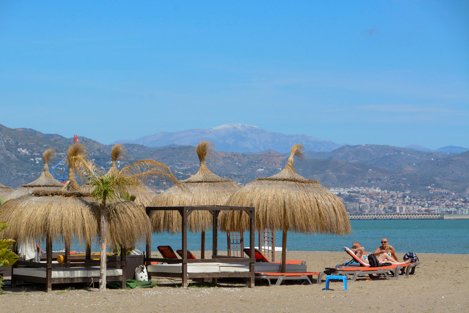 Sonnenschirme mit Badegästen vor Gebirge am Strand von Málaga