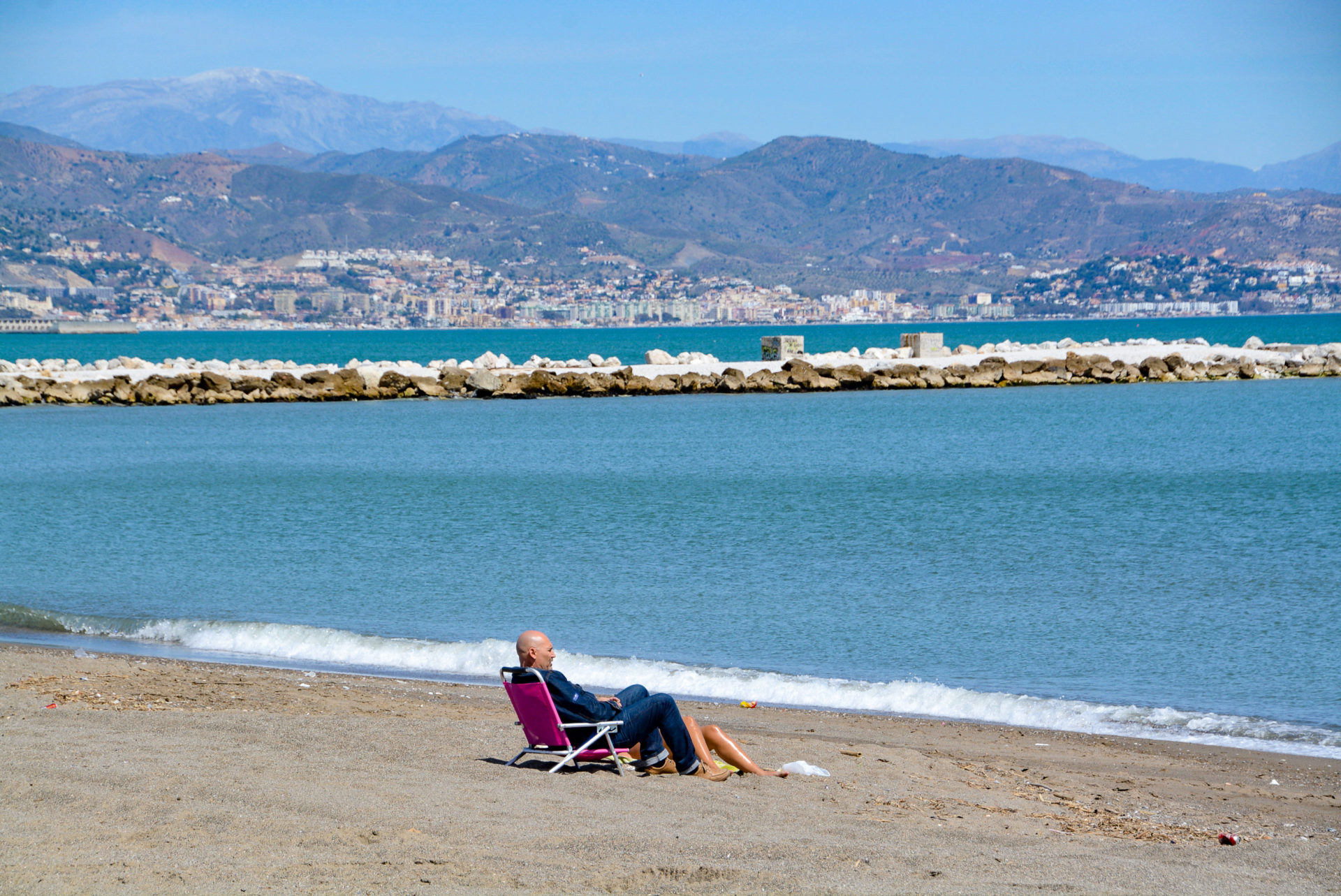 Badegast im Strandstuhl mit Blick aufs Meer in Málaga und das Gebirge