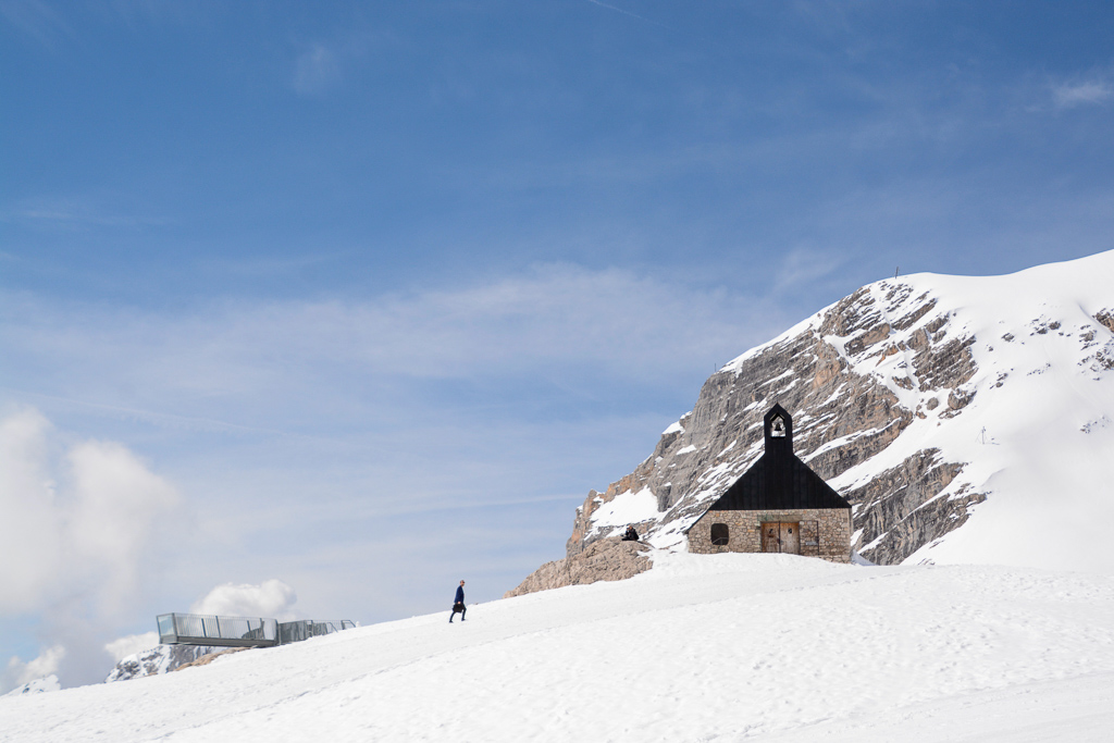 Mann mit Aktentasche geht durch den Schnee zur Kapelle auf der Zugspitze
