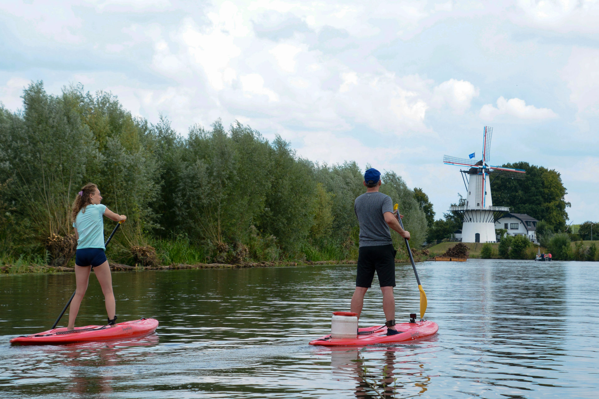 Mann und Frau auf Stand-up-paddles auf dem Fluss Linge mit Windmühle im Hintergrund