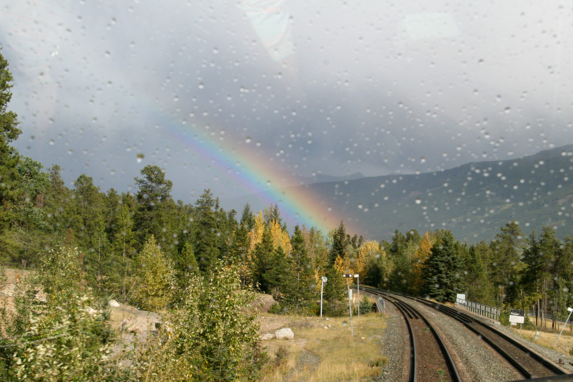 Regenbogen über den Gleisen zwischen Vancouver und Toronto mit Bergen im Hintergrund
