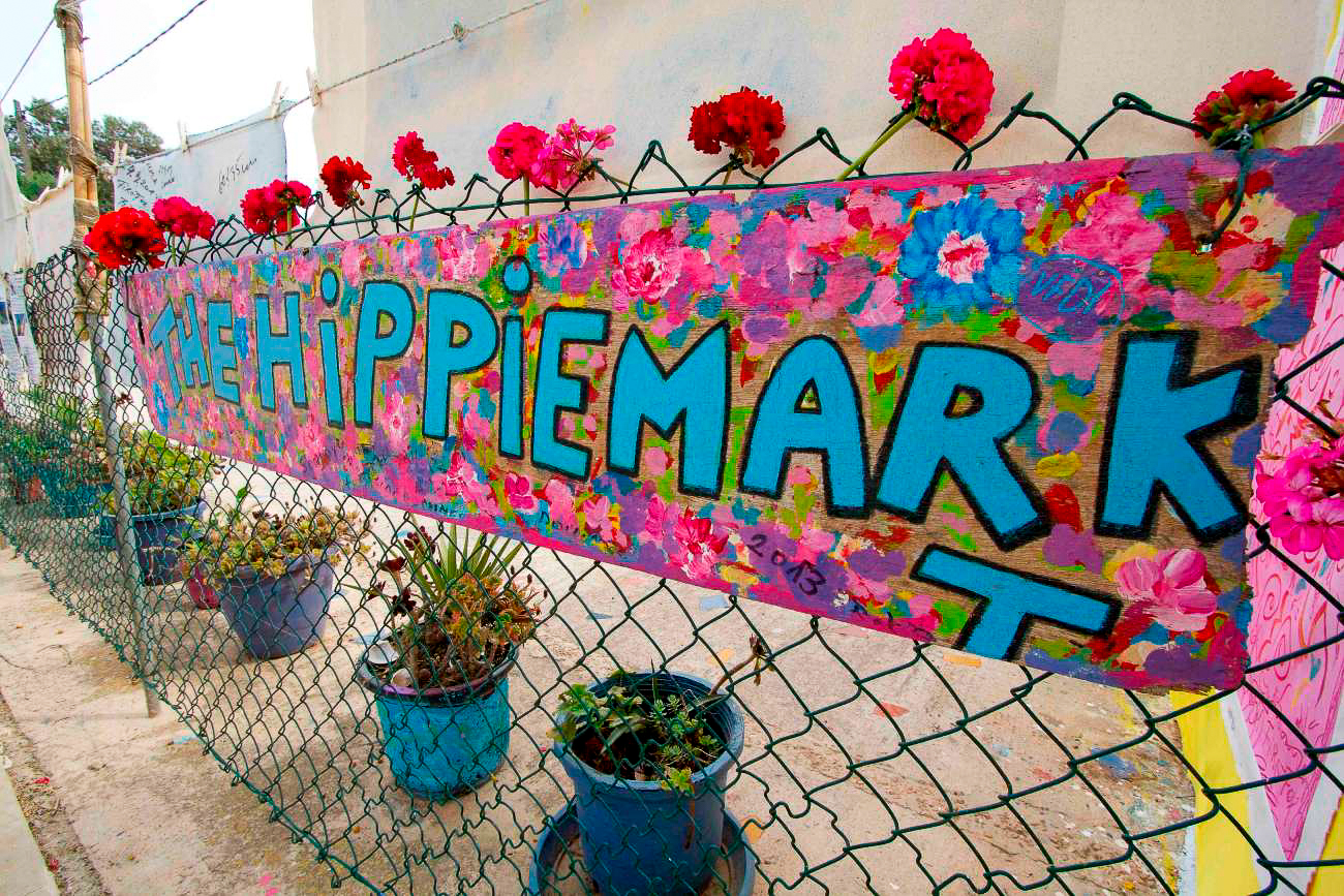 Blumen verzieren ein Schild, das auf den Hippiemarkt von Formentera aufmerksam macht