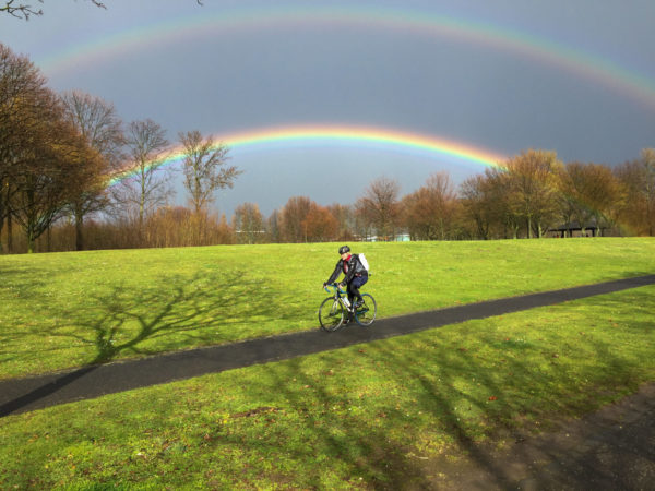 Radfahrer mit doppeltem Regenbogen im Beueler Teil der Rheinaue
