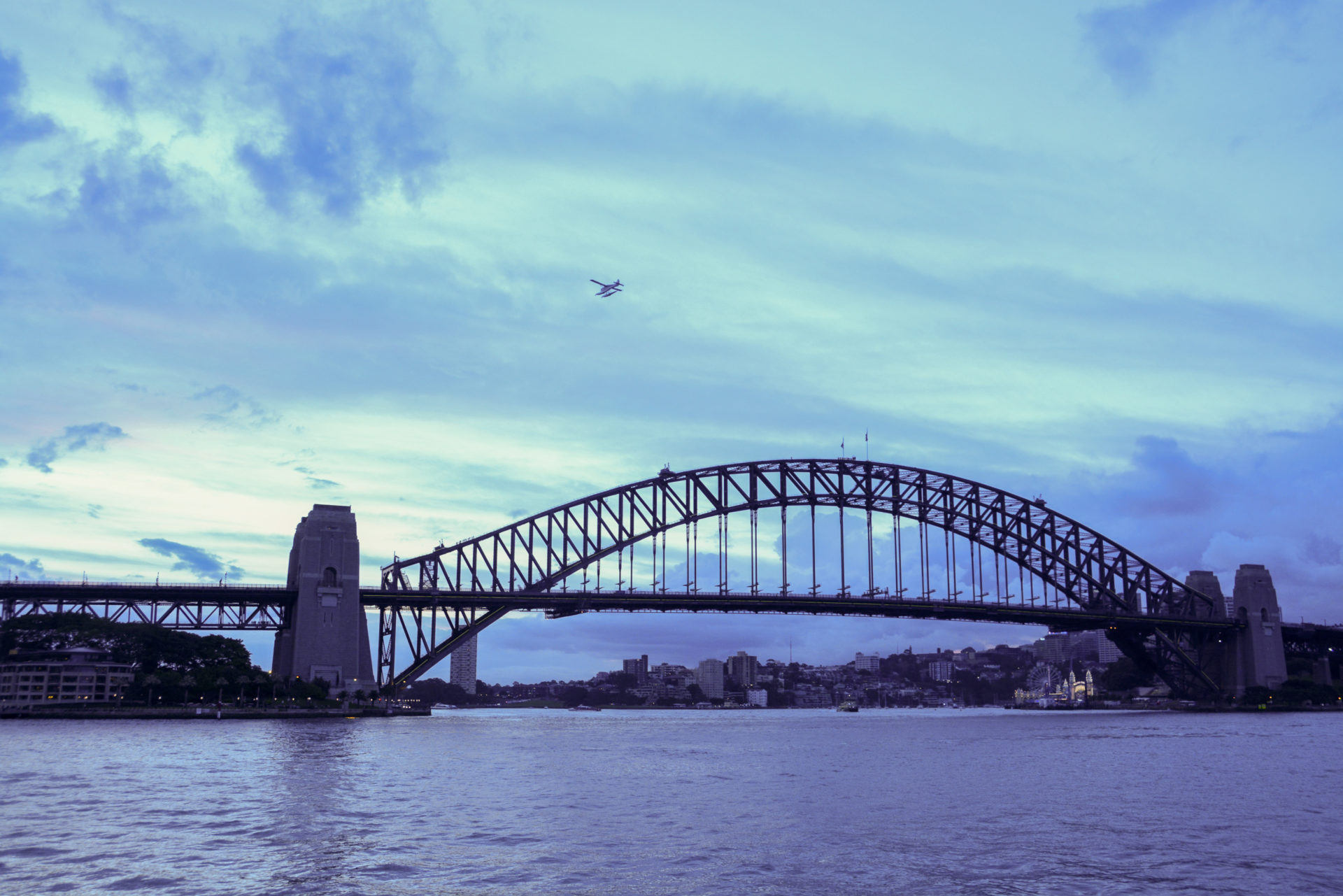 Wasserflugzeug über der Harbour Bridge in Sydney im Abendlicht