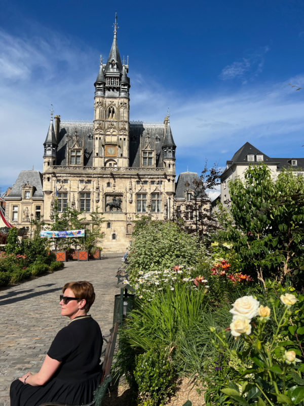 Junge Frau vor einem Blumengarten und dem ehrwürdigen Rathaus der nordfranzösischen Stadt Compiegne