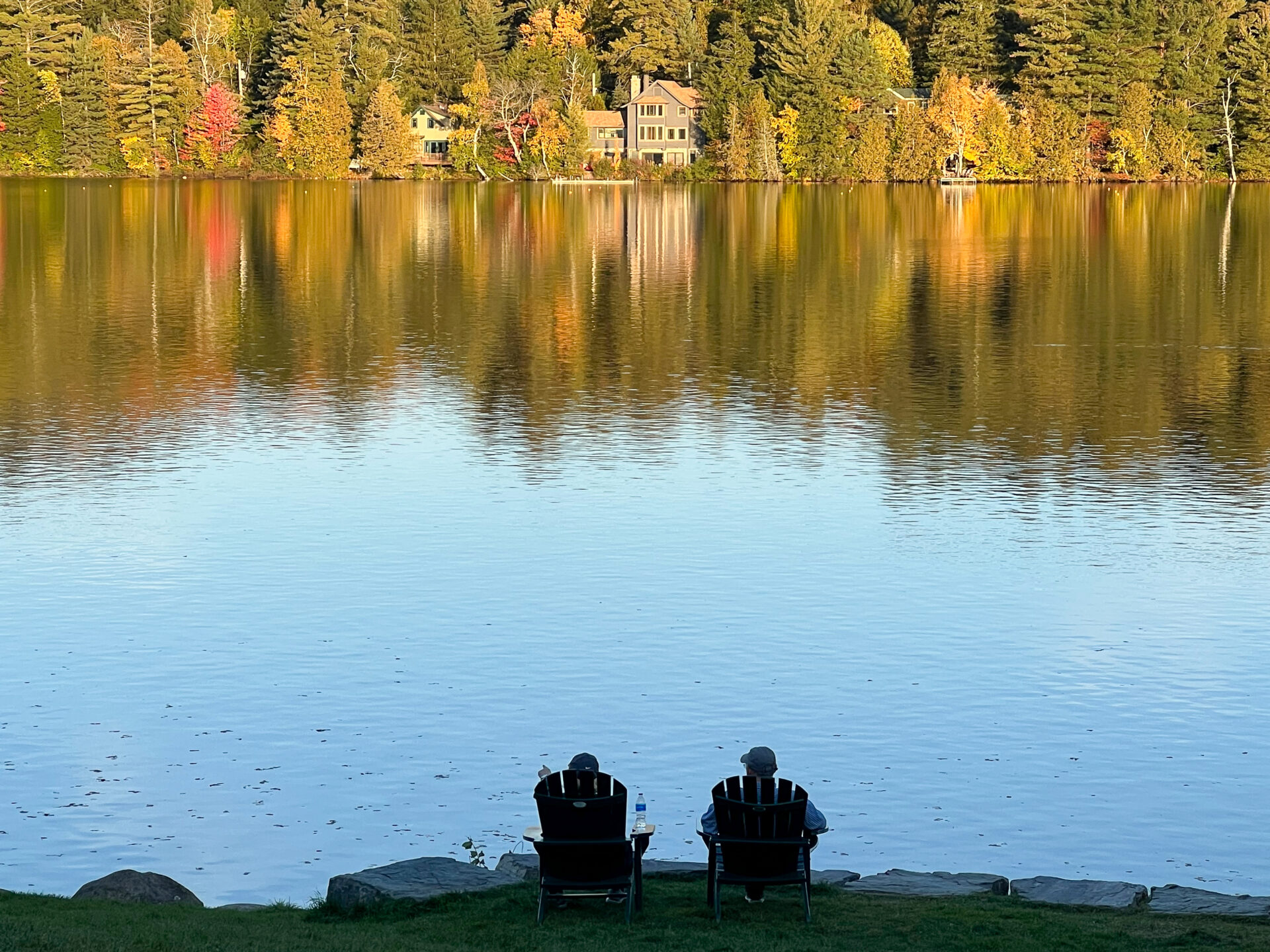 Zwei Menschen sitzen in Adirondack Stühlen und blicken auf den Mirror Lake in Lake Placid