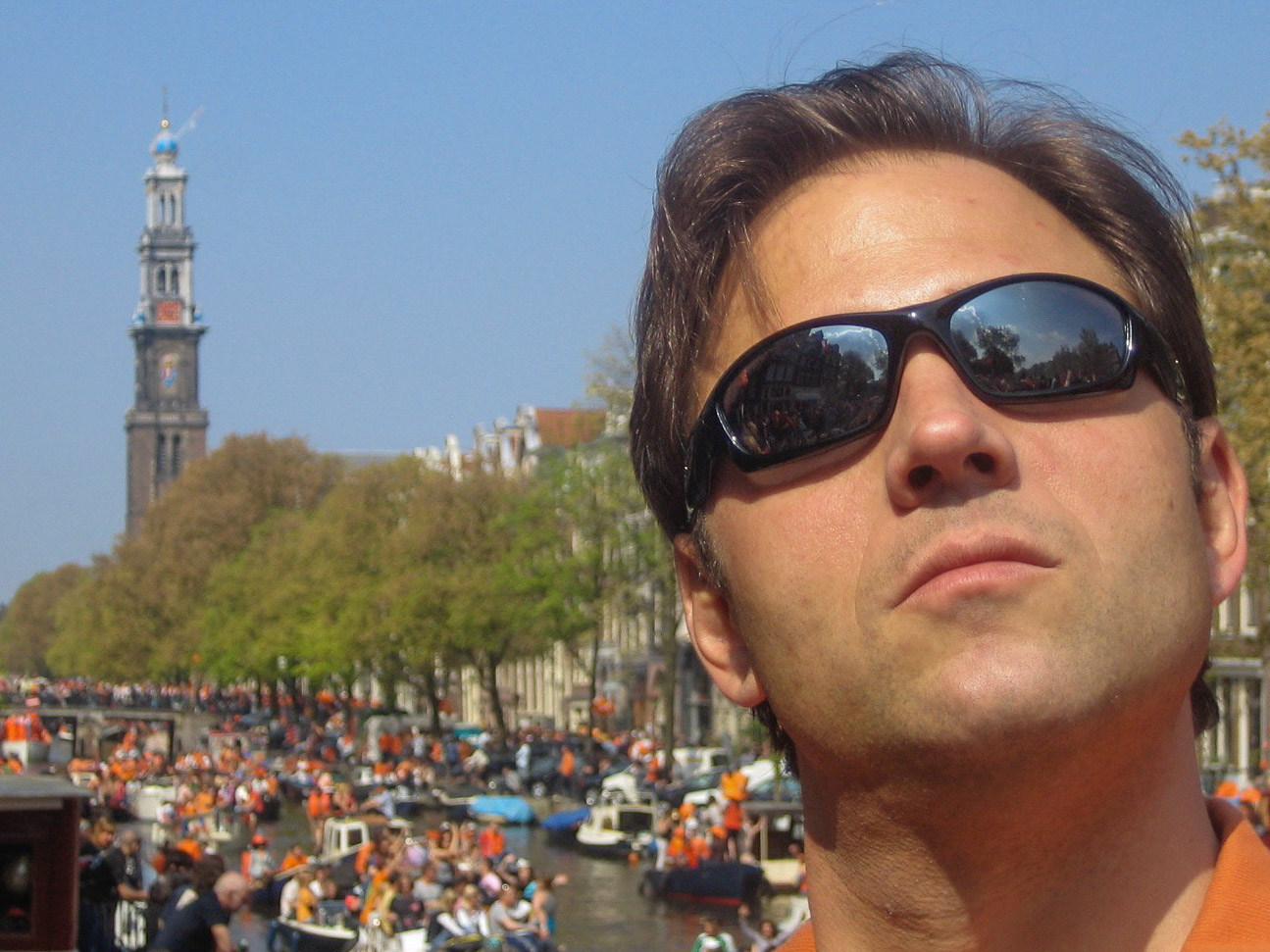 Mann mit Sonnenbrille auf einer Brücke in Amsterdam mit Westerkerk im Hintergrund