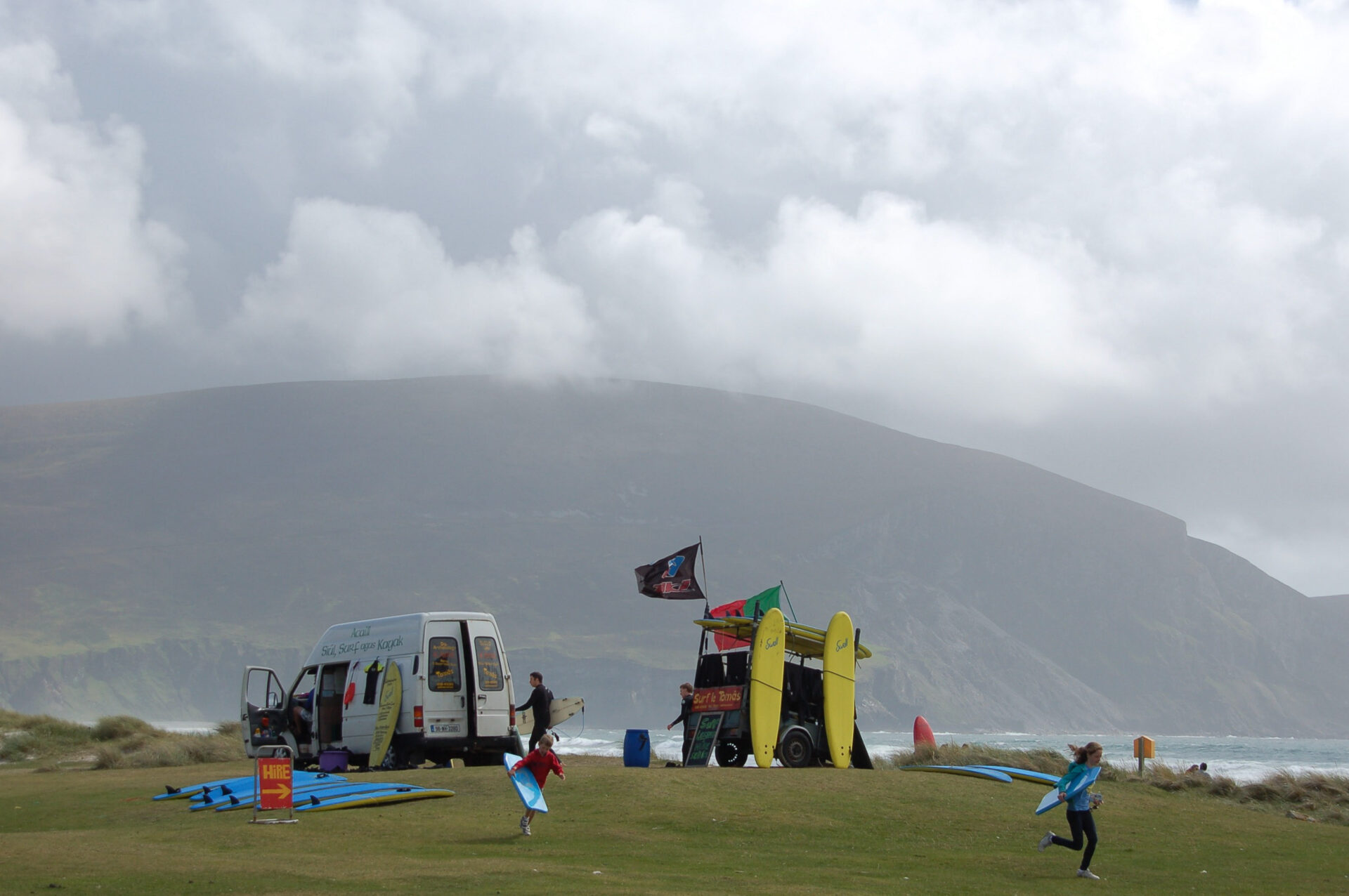 Transporter und Anhänger mit Surfbrettern und Kindern vor einem Berg auf Achill Island in Irland