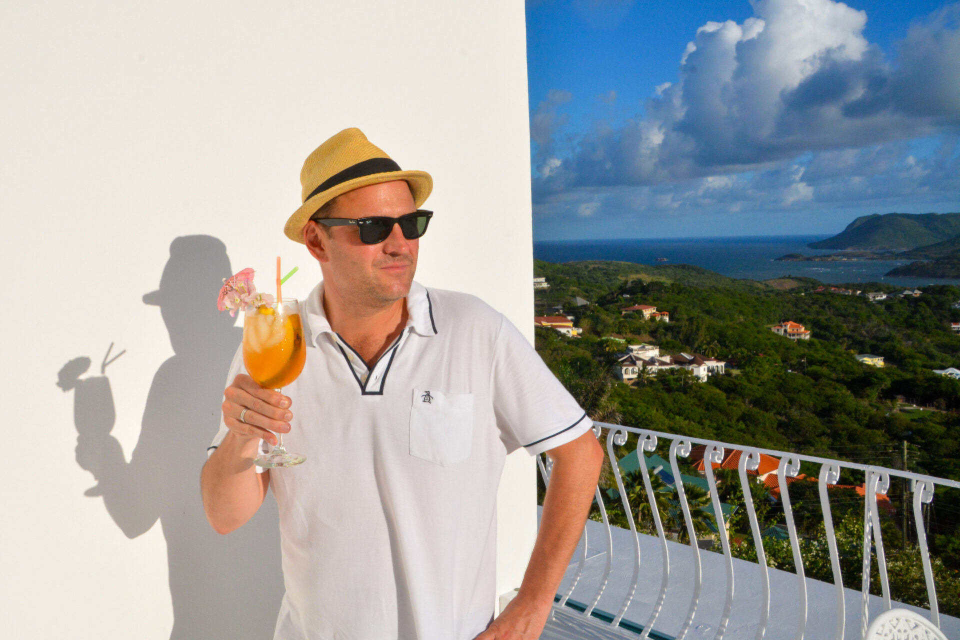 Mann mit Hut Cocktail und Sonnebrille auf einem Balkon hoch über der Insel St. Lucia in der Karibik