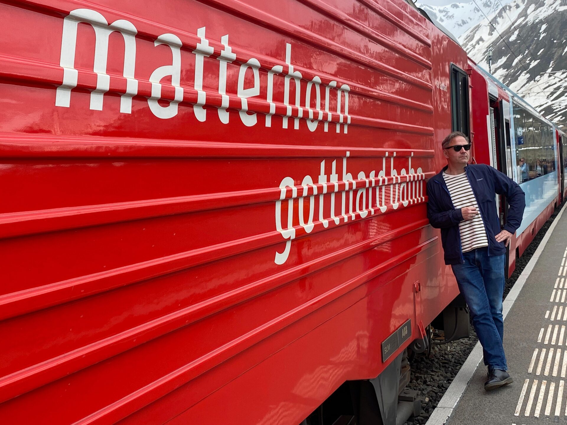 Mann lehnt gegen die Lokomotive der Matterhorn Gotthard Bahn
