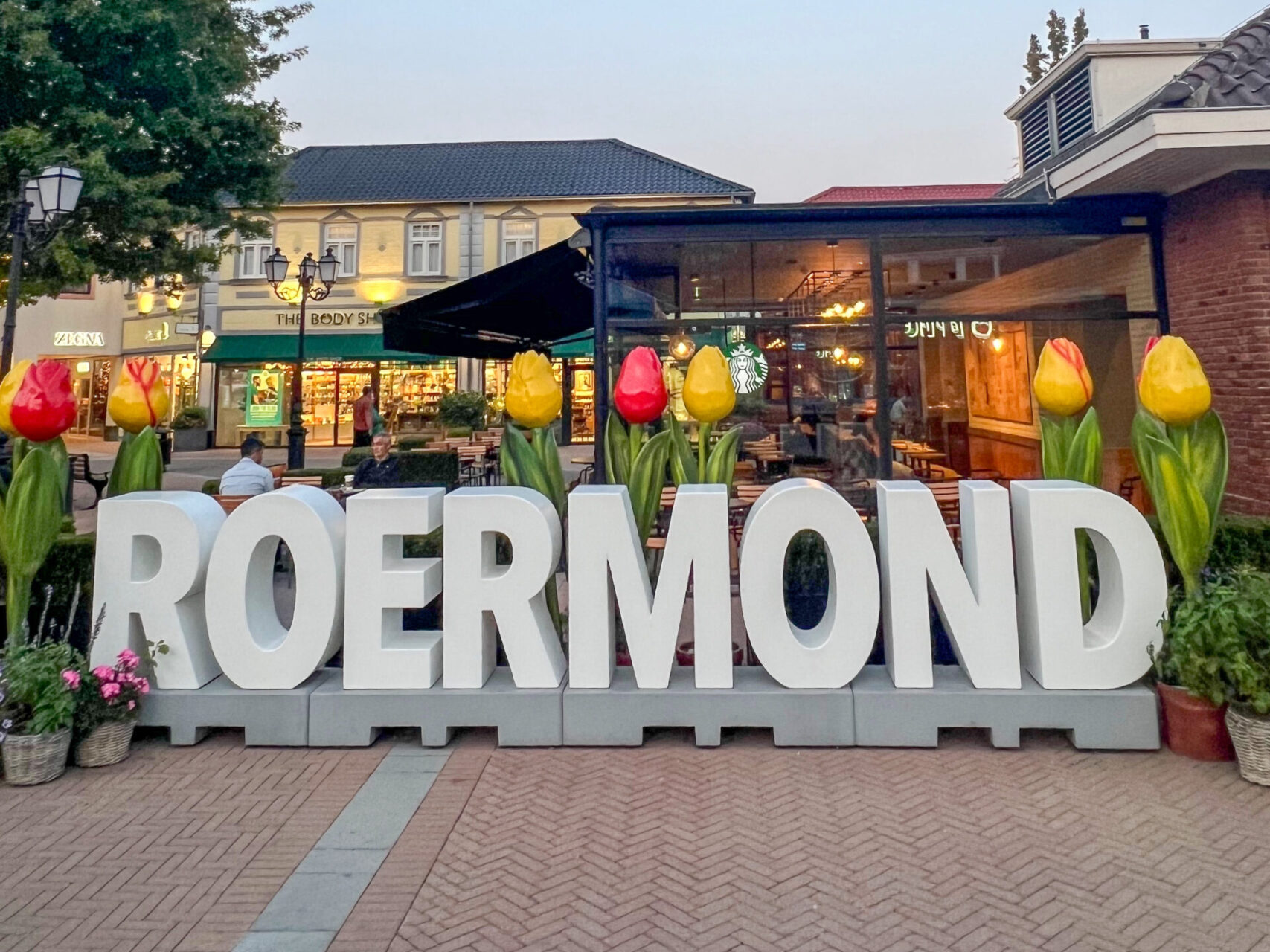 Schriftzug der niederländischen Stadt Roermond vor Geschäften im Outlet Center