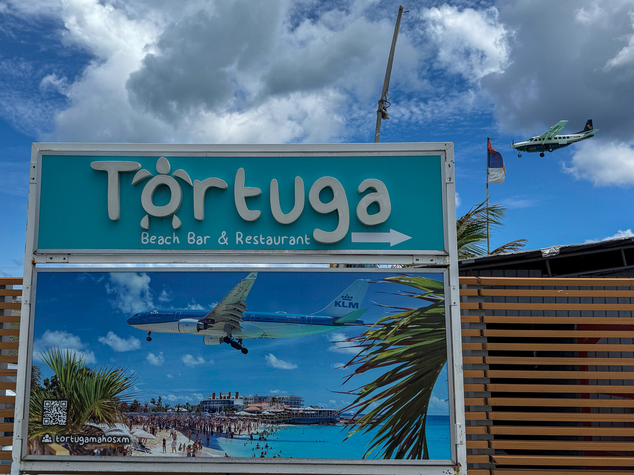 Propellermaschine im Anflug auf den Flughafen von Sint Maarten und Schild mit einem Riesenjet der KLM