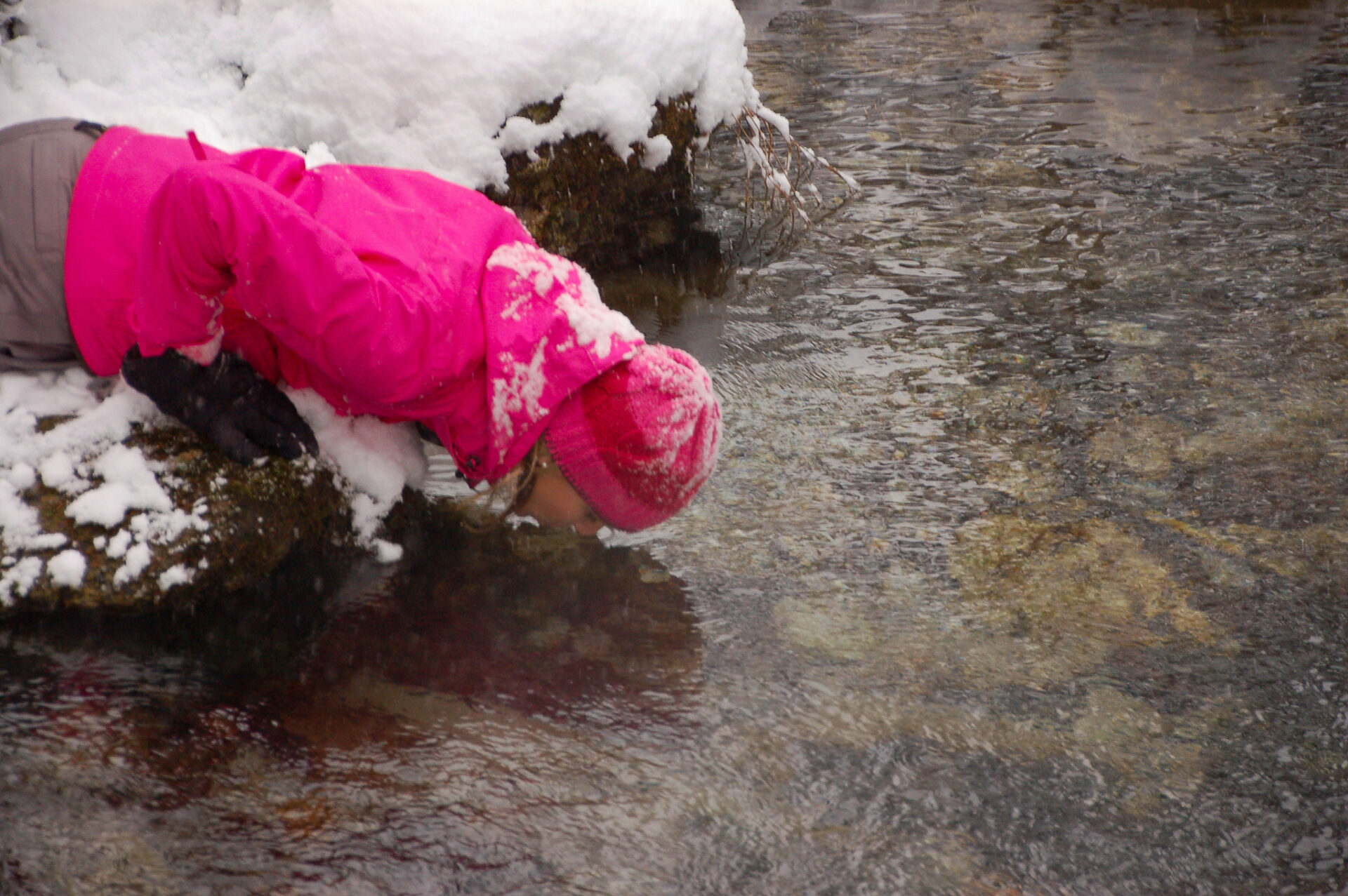 Frau mit pinker Jacke trinkt Wasser aus einem Bach in Gastein