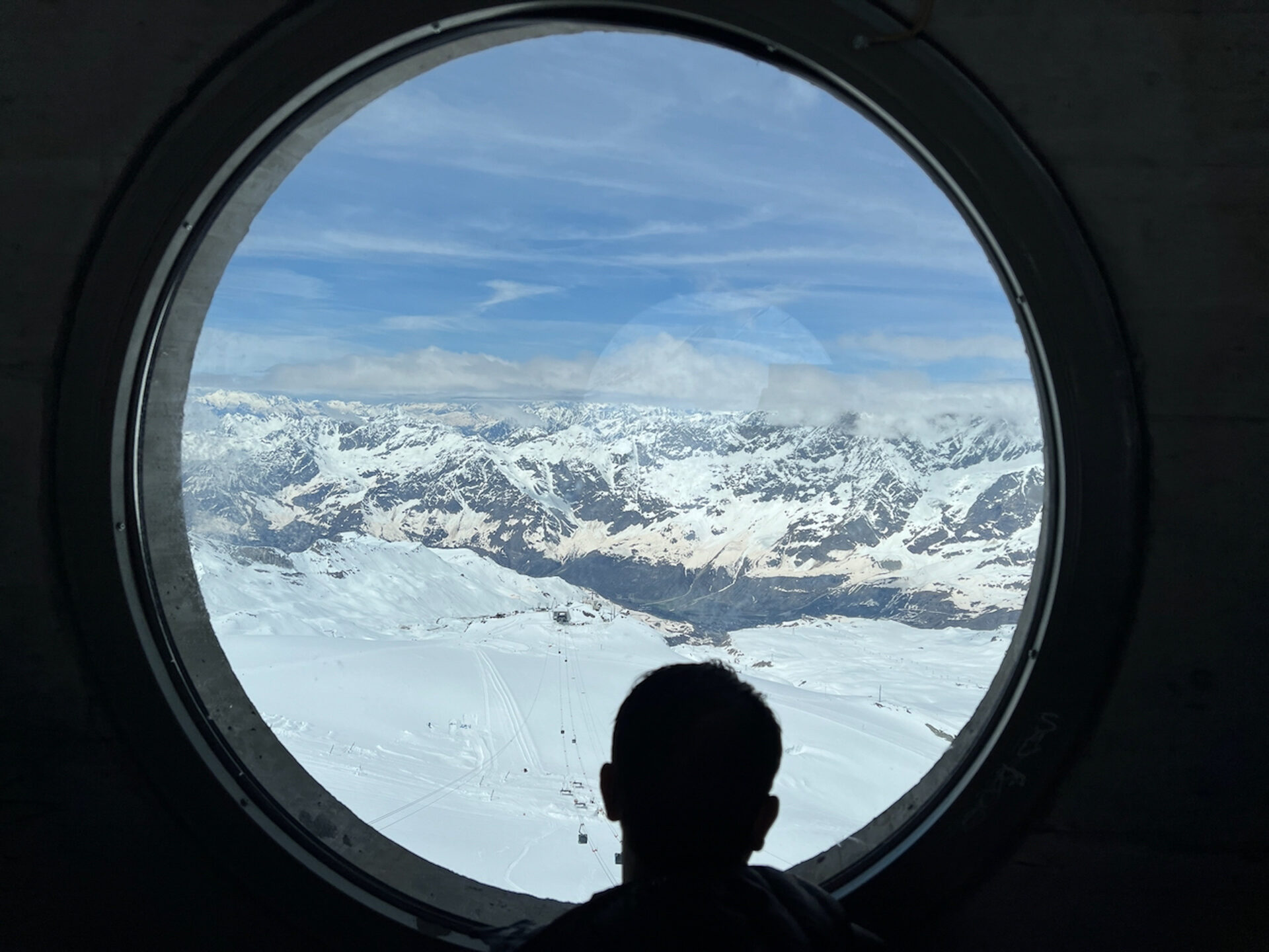 Mann blickt durch ein Bullauge auf die Bergwelt der Matterhorn Glacier World